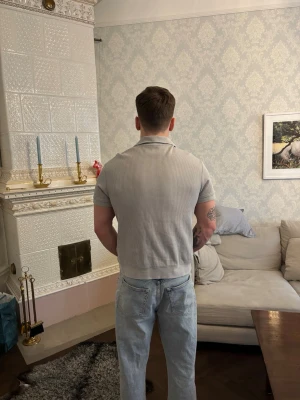 Ljusgrå ribbad pikétröja - Säljer en ljusgrå ribbad pikétröja med krage och korta ärmar. Tröjan har en relaxed passform och är tillverkad i ett mjukt bomullsmaterial. Perfekt för en clean och stilren look. Aldrig använd!