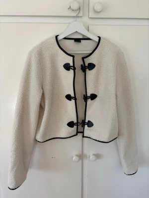 Vit teddyjacka/overshirt från Gina Tricot - Säljer en snygg vit teddyjacka/overshirt från Gina Tricot med svarta detaljer och knäppningar framtill. Jackan har rund halsringning, långa ärmar och är kantad med svart fuskskinn. Storlek M🩷