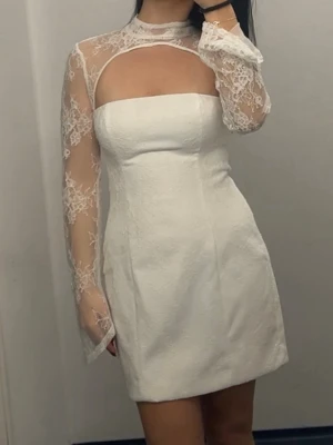 Student klänning , Vit klänning  - Kort vit klänning med figurnära passform och långa spetsärmar. Materialet är en mix av spets och tyg med struktur. 