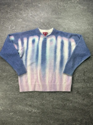 Blå Supreme stickad tröja med mönster - Supreme stickad tröja i blått med unikt gradientmönster i vitt, rosa och lila. Rund halsringning, ribbade muddar och nederkant. Tröjan har en oversized vibe och är tillverkad i mjukt material som känns lyxigt och trendigt.