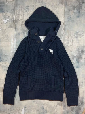 Mörkblå hoodie från Abercrombie & Fitch - Först till kvarn! Detta är en mysig mörkblå hoodie i grovstickat material från Abercrombie & Fitch. Har huva med dragsko, knappar vid halsen och en ficka framtill. Den är vintage och är väldigt svår att få tag på, jag tror inte man kan gå fel här. A&F logga broderad på bröstet ger en clean look. Perfekt för chill dagar och snygg till jeans. Den är vad jag sett helt fläckfri och har inga hål eller slitningar. Storleken: XL men sitter mer som en M/L. Hör av dig vid frågor! Kan även diskutera pris.