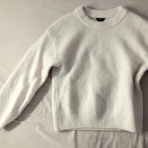 Vit mjuk stickad tröja  - Klassisk vit stickad tröja med rund halsringning och ribbade muddar vid ärmslut och nederkant. Tröjan har en enkel och stilren design, perfekt för lager på lager och passar till det mesta. Materialet känns mjukt och bekvämt.