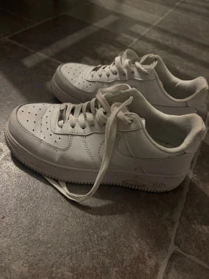 Vita Nike Air Force 1 sneakers - Behöver torkas av, och sula saknas inuti. Därav pris. Men hela! Och skit snygga! Storlek 39. Klassiska vita Nike Air Force 1 sneakers i lågt utförande. Skorna har en stilren design med perforerad tå, vita skosnören och sula i gummi. Tillverkade i läder med diskret Nike-logga på sidan och metallbricka med 'AF1' på snörningen.