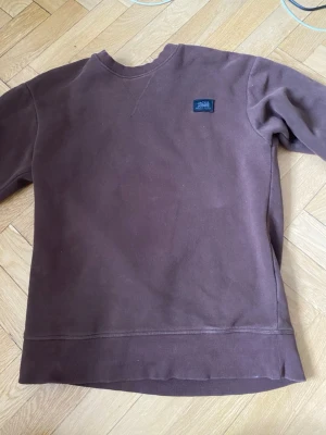 Brun sweatshirt från Jack & Jones - Mysig brun sweatshirt från Jack & Jones med rund halsringning och ribbade muddar. Tröjan har en liten blå logotyp-patch på bröstet och är tillverkad i mjukt bomullsmaterial. Perfekt för en avslappnad och stilren look.