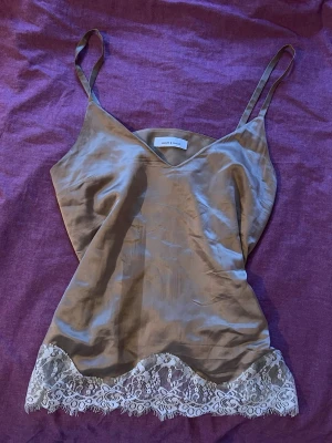 Linne med spets  - Beige guldig silkes topp från Samsoe samsoe  i glansigt material med tunna axelband och v ringning. Vit spetskant längst ner o funkar att stylea till jeans eller ha som nattlinne🥰 