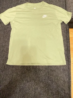 Grön Nike T-shirt i bomull - Snygg grön T-shirt från Nike med klassisk vit logga på bröstet. Tillverkad i mjuk bomull och har en enkel, rak passform med korta ärmar och rund halsringning. Perfekt för en avslappnad och sportig stil.