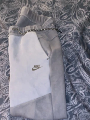 Gråa mjukisbyxor från Nike - Snygga grå mjukisbyxor från Nike med klassisk logga på benet. Byxorna har resår i midjan och dragsko för bästa passform. Tillverkade i mjukt material som är perfekt för chill eller träning. Enkel och stilren design som funkar till det mesta.