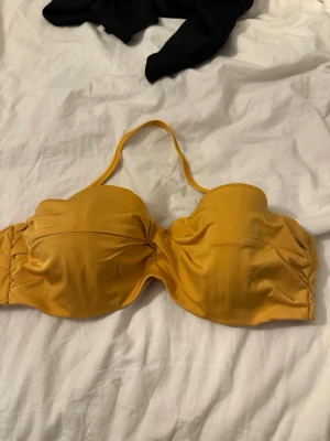 Gul bandeau bikiniöverdel - Snygg gul bandeau bikiniöverdel med avtagbara axelband och vadderade kupor. Bikinin har en enkel och stilren design med lätt rynkade detaljer på sidorna. Perfekt för soliga dagar på stranden. Går att köpa toppen försig