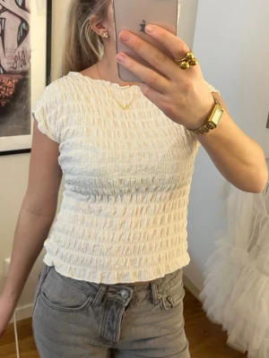 Vit ribbad topp med kort ärm - Säljer en söt vit ribbad topp med korta ärmar och stretchigt smockat tyg.