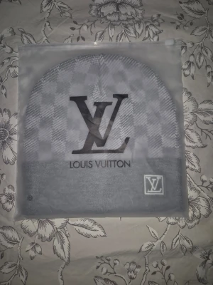 Grå Louis Vuitton mössa - Snygg grå mössa från Louis Vuitton med klassiskt rutmönster och stor LV-logga framtill. Mössan har vikt kant med en liten LV-patch på sidan. Tillverkad i mjukt stickat material som känns skönt mot huden. Perfekt accessoar för dig som gillar exklusiv streetstyle.