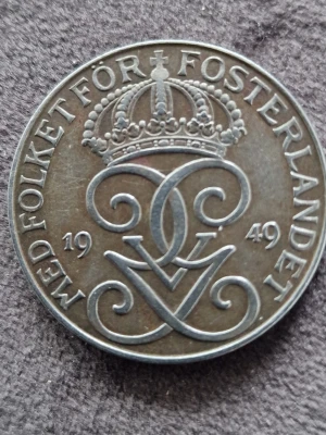 Svenskt 5 öre mynt 1949 - Säljer ett svenskt 5 öre mynt från 1949 i bronsfärg. Ena sidan har tre kronor och texten 'FEM ÖRE', andra sidan har kunglig krona, monogram och texten 'MED FOLKET FÖR FOSTERLANDET'. Perfekt för samlare av gamla mynt.