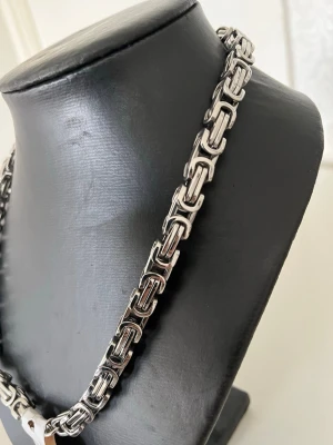 Tungt kedjehalsband i silverfärg - Snyggt halsband med robust kedjedesign i silverfärgad metall. Länkarna är rektangulära och ger ett modernt, industriellt intryck. Perfekt för dig som vill ha ett statement-smycke som sticker ut. Passar både till streetwear och mer stilrena outfits.