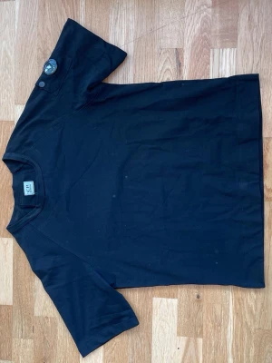 Svart t-shirt från C.P. Company - Svart t-shirt från C.P. Company med klassisk passform och rund hals. T-shirten har korta ärmar och en ikonisk linsdetalj på ena ärmen. Tillverkad i mjuk bomull som känns skön mot huden. Perfekt för en clean och stilren look. Priset kan diskuteras för seriösa köpare. Och det är M passar S