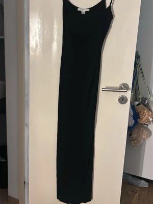 Svart långklänning med smala band - En stilren svart långklänning med smala axelband och rak passform. Klänningen har en enkel och tidlös design som passar perfekt till olika tillfällen. Materialet känns mjukt och följsamt mot kroppen.