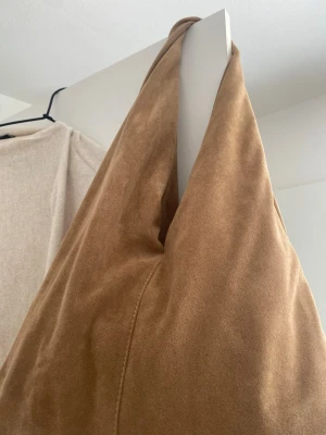 Beige axelremsväska från Gina Tricot - Snygg beige axelremsväska från Gina Tricot i mjukt mockaimitationsmaterial. Väskan har en slouchy form och bred axelrem, perfekt för dig som gillar en avslappnad men trendig look. Enkel design utan synliga detaljer förutom en knappstängning.