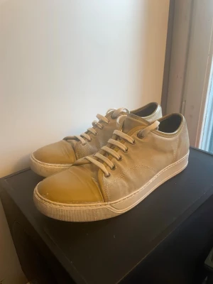 Beige sneakers med lackad tå - Stilrena Lanvins i beige mocka med glansig, lackad tå i olivgrönt. Skorna har vita snören, vita sulor och diskreta sömmar. Perfekta för dig som gillar en unik twist på klassiska sneakers.
