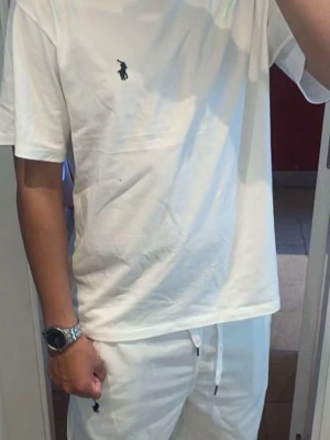 Vit t-shirt från Ralph Lauren - Vit t-shirt från Ralph Lauren med klassisk passform och korta ärmar. T-shirten har en liten broderad logotyp i svart på bröstet och är tillverkad i mjuk bomull. Perfekt för en clean och stilren look.