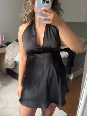 Svart satinliknande halterneckklänning - Snygg svart kortklänning i satin med halterneck och öppen rygg från Zara. Har sytt vid urringningen så att den inte är lika ljup, men det går att sprätta upp💞