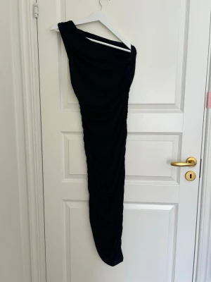 Svart oneshoulder långklänning - Säljer en svart långklänning med oneshoulder-design. Klänningen har en åtsittande passform och är gjord i ett mjukt, stretchigt material som ger en snygg drapering längs kroppen. Perfekt för dig som vill ha en stilren och trendig look.