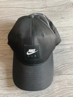 Svart Nike Air keps - Snygg svart keps från Nike Air med klassisk böjd skärm och justerbar baksida. Kepsen har en tydlig Nike Air-logga framtill och är tillverkad i ett lätt, slitstarkt material som passar perfekt till streetwear-stilen . Köpt i london.