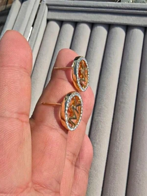 Guldiga MK örhängen med stenar - Säljer ett par snygga örhängen i guldton. Örhängena är runda med MK-logga i mitten och har gnistrande stenar runt hela kanten för extra bling. Perfekta för dig som gillar statement-accessoarer och vill ha något som sticker ut.