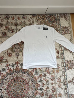 Polo Ralph Lauren - tröja - Vit långärmad sommar tröja från Polo Ralph Lauren i klassisk passform. Tillverkad i mjuk bomull med rund hals och liten broderad logga på bröstet. Enkel och stilren design. Storlek M