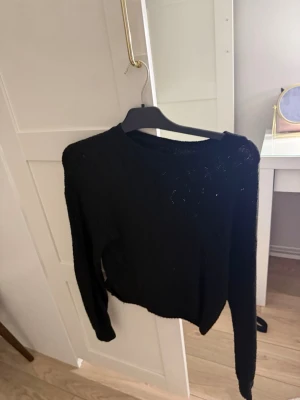 Svart stickad tröja  - Snygg svart stickad tröja med detaljer. Tröjan har rund halsringning och långa ärmar, perfekt för att lyfta en enkel outfit. Mjuk och bekväm passform som funkar året runt.