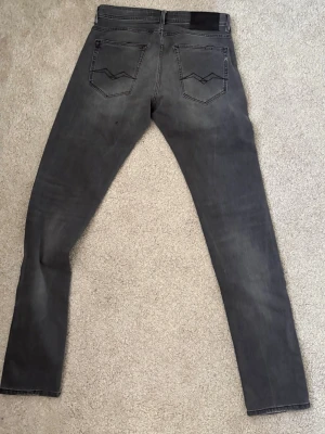 Replay jeans - W 30 L 33 Snygga grå jeans med klassisk femficksdesign och diskreta slitningar. Jeansen har svarta sömmar och en liten logotyp på fickan. Tillverkade i stretchigt denim för skön passform och stilren look.