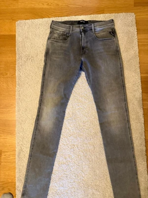 Grå slim fit jeans från Replay - Säljer ett par gråa slim fit jeans från Replay med klassisk femficksdesign och snygga detaljer på bakfickan. Jeansen har normal midja och är tillverkade i stretchigt denimtyg för extra komfort. Perfekta för en avslappnad och trendig look. Storlek W32/L34 aldrig använda 