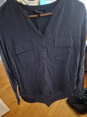 Mörkblå skjorta från kappahl - Mörkblå skjorta från kappahl med två bröstfickor och knappar framtill. Skjortan har lång ärm och en avslappnad passform, perfekt för en chill och stilren look.