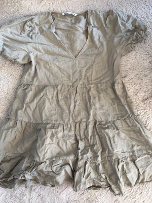 Grön kort klänning från Zara - Supersöt beige kort klänning från Zara i luftig linnemix. Klänningen har v-ringning, korta puffärmar och volangdetaljer i kjolen. 