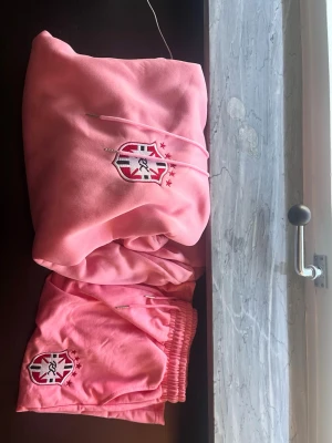 Rosa loungewear-set med hoodie - Mysigt rosa loungewear-set från FC BRASIL  med matchande hoodie och shorts. Båda plaggen har klubbens logga broderad framtill. Hoodien har magficka och dragsko i huvan. Perfekt för chill dagar hemma.