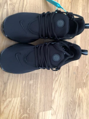 Svarta Nike Air Presto sneakers - Snygga helsvarta Nike Air Presto sneakers med klassisk låg siluett. Skorna har en ovandel i mesh och syntet, rund tå och Nike-logga på sidan och tungan. Gummisula för bra grepp och komfort. Perfekta för en sportig och stilren look.