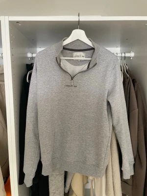 Grå halvzip tröja Cerruti 1881 - Ljusgrå sweatshirt från Cerruti 1881 med halv dragkedja och broderad logga på bröstet. Tröjan har ribbade muddar vid ärmslut och nederkant samt en avslappnad passform. Tillverkad i mjukt material för extra komfort.