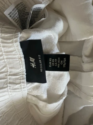 Vita linneshorts från H&M - Säljer ett par vita shorts från H&M i regular fit. De har elastisk midja och är tillverkade i en skön blandning av linne och viskos. Shortsen har en bakficka och en enkel, clean design som passar perfekt till sommaren.