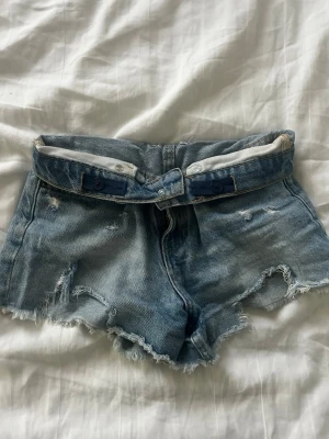 Blå midwaist jeansshorts från Zara - Skriv innan ni köper!!🩷.                                     Säljer ett par blå jeansshorts med råa, fransiga kanter och slitna detaljer. Shortsen är midwaist och kan både knäppas upp och även vikas ner som ser superfint ut. Perfekta för sommardagar och festivaler. 🩷