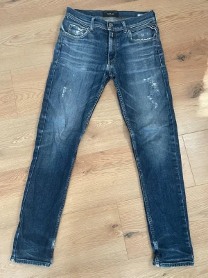 Mörkblå jeans från Replay - Snygga mörkblå jeans från Replay med slitna detaljer och klassisk femficksdesign. Jeansen har en smal passform och är tillverkade i stretchigt denim för extra komfort. Perfekta för en trendig och avslappnad stil.