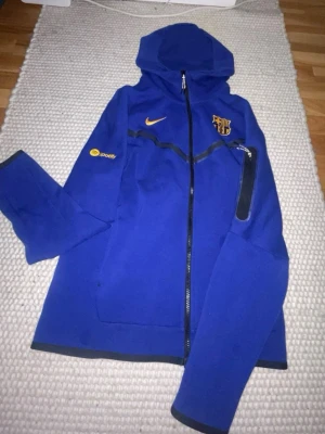 Blå FC Barcelona hoodie Nike - Snygg blå hoodie från Nike med FC Barcelona-logga och Spotify-detalj på ärmen. Dragkedja framtill, huva och svart detalj på ena ärmen. Perfekt för dig som gillar fotboll och vill ha en sportig stil.äkta för 1300 är hellt oanvänd eftersom det it passar mig jsg fick den på min födelsedag och den va från mall of scandinavia nike så hellt äkta dkriv om mer bilder priset kan diskuteras om ni vill