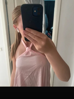 Ljusrosa halterneck topp med knyt - Säljer en söt ljusrosa halterneck topp med knyt i nacken. Toppen är ärmlös och har en lös passform som ger en avslappnad vibe. Perfekt till sommaren och enkel att styla med jeans eller kjol.