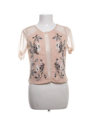 Rosa meshblus med broderi - Söt rosa meshblus med korta ärmar och transparent linje i mitten. Framsidan har broderade blommor i vitt och grönt samt dekorativa vågiga sömmar. Blusen har rund halsringning och luftig passform.