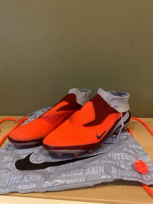 Nike fotbollskor elit  - Säljer ett par Nike Phantom GT Elite AG-Pro  använda två gånger fotbollsskor i rött och ljusblått med svarta detaljer. Skorna har strumpliknande skaft och är tillverkade i syntetmaterial för bästa grepp och kontroll på planen. Perfekta för konstgräs och avancerat spel.