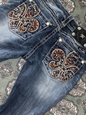 Miss Me jeans med broderade fickor - Säljer ett par blå Miss Me jeans med slitningar och stora broderade bakfickor dekorerade med paljetter och nitar. Jeansen har en låg midja och kontrastsömmar som ger en cool look. Perfekta för dig som gillar detaljer och statement-plagg.