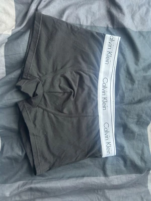 Svarta kalsonger från Calvin Klein - Snygga svarta kalsonger från Calvin Klein med vit resår och tydlig logga runt midjan. Tillverkade i mjuk bomullsblandning för skön passform och stilren look. Perfekta för dig som gillar klassisk design och hög komfort.