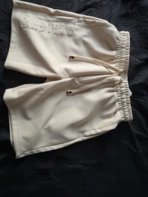 Beiga shorts med snörning från Artefact - Säljer ett par beiga shorts från Artefact med broderad logga framtill. Shortsen har elastisk midja med snörning och en bakficka. Perfekta för chill dagar och har en relaxed fit.