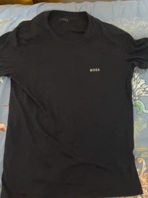 Svart t-shirt från BOSS - Snygg svart t-shirt från BOSS med diskret logga på bröstet. Klassisk rund halsringning och normal passform. Tillverkad i mjuk bomull som känns skön mot huden. Perfekt basplagg för en clean och stilren look.