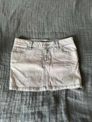 Ljus lågmidjad jeanskjol  - Snygg kort jeanskjol med klassiska fem fickor, bälteshällor och knappstängning fram. Kjolen har en enkel och stilren design, perfekt till sommaren. Materialet är denim och kjolen har en normal passform.