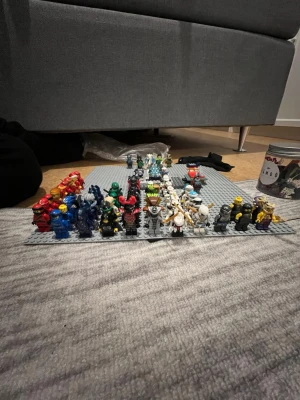 Samling LEGO minifigurer på platta - Stor samling LEGO minifigurer i olika färger och stilar, uppställda på en grå LEGO-platta. Figurerna inkluderar bland annat röda, blå, gröna, svarta och vita karaktärer, vissa med hjälmar och tillbehör. Perfekt för dig som gillar att bygga och samla LEGO.Det är även Lego byggen och kom gärna med bud