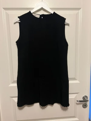 Svart ärmlös klänning från Allday - Svart klänning från Allday med enkel, rak passform och ärmlös design. Klänningen har rund halsringning och plisserad nederkant som ger en snygg detalj. Perfekt för dig som gillar stilrena plagg med en twist.