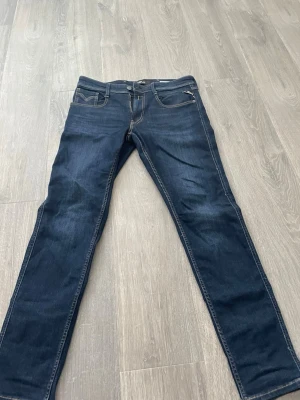 Mörkblå slim fit jeans från replay - Snygga mörkblå slim fit jeans från replay med klassisk femficksdesign och kontrastsömmar. Jeansen har dragkedja och knapp i midjan samt en liten myntficka fram. Perfekta för dig som gillar en smalare passform.
