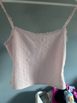 Ljusrosa spetslinnetopp - Söt ljusrosa linnetopp med tunna axelband och spetskant upptill. Toppen har ett broderat hålmönster över hela tyget som ger en romantisk vibe. Perfekt till sommaren och enkel att matcha med jeans eller kjol.